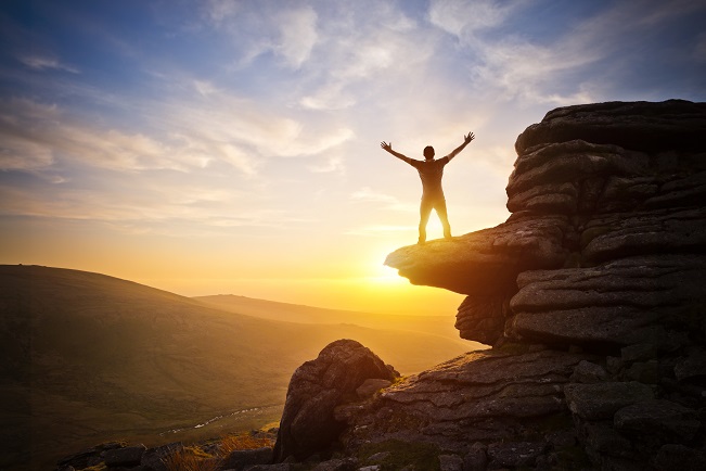 guy on a rock reaching the sunset