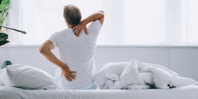 an old man sitting on a bed with back pain