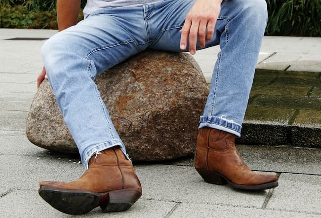 man sitting on a stone wearing blue jeans and country boots