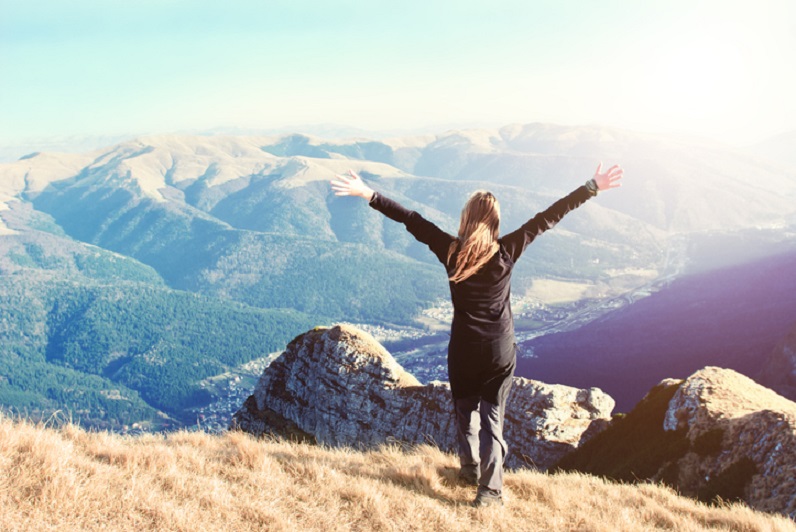 young woman standing on top of mountain with arms outstretched