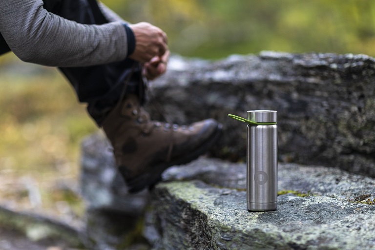 picture of person tying his boots beside a stainless steel bottle on the rocks