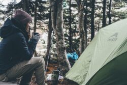 picture of a woman sitting in the woods beside a tent