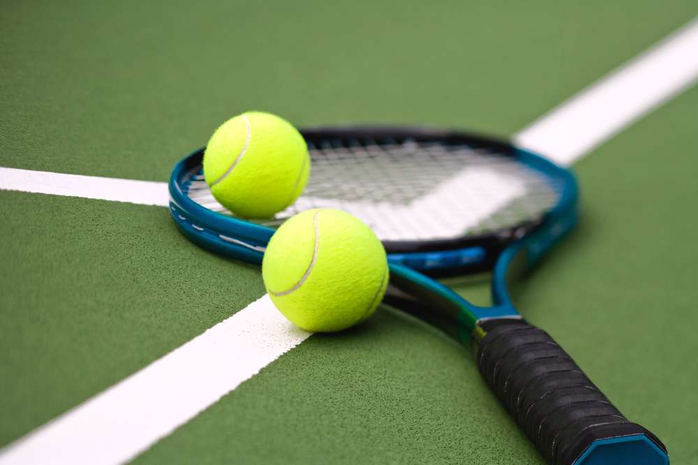 Tennis Racquet on the gorund with two tennis balls