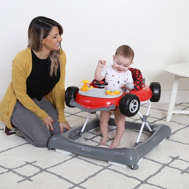 picture of a woman sitting on the ground beside a baby in an activity walker