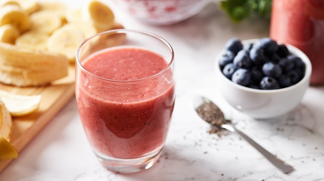 a pre-workout shake in a glass placed on a marble table next to other healthy foods