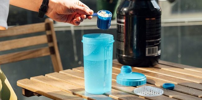 guy putting a scoop of protein powder in a blue shaker