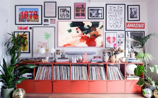 a lo of frames on a wall and a red shelf with a lot of books 