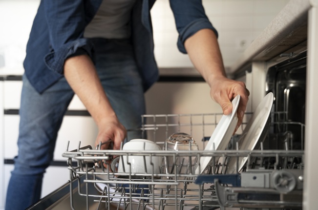 A man in front of an open dishwasher puts down dishes